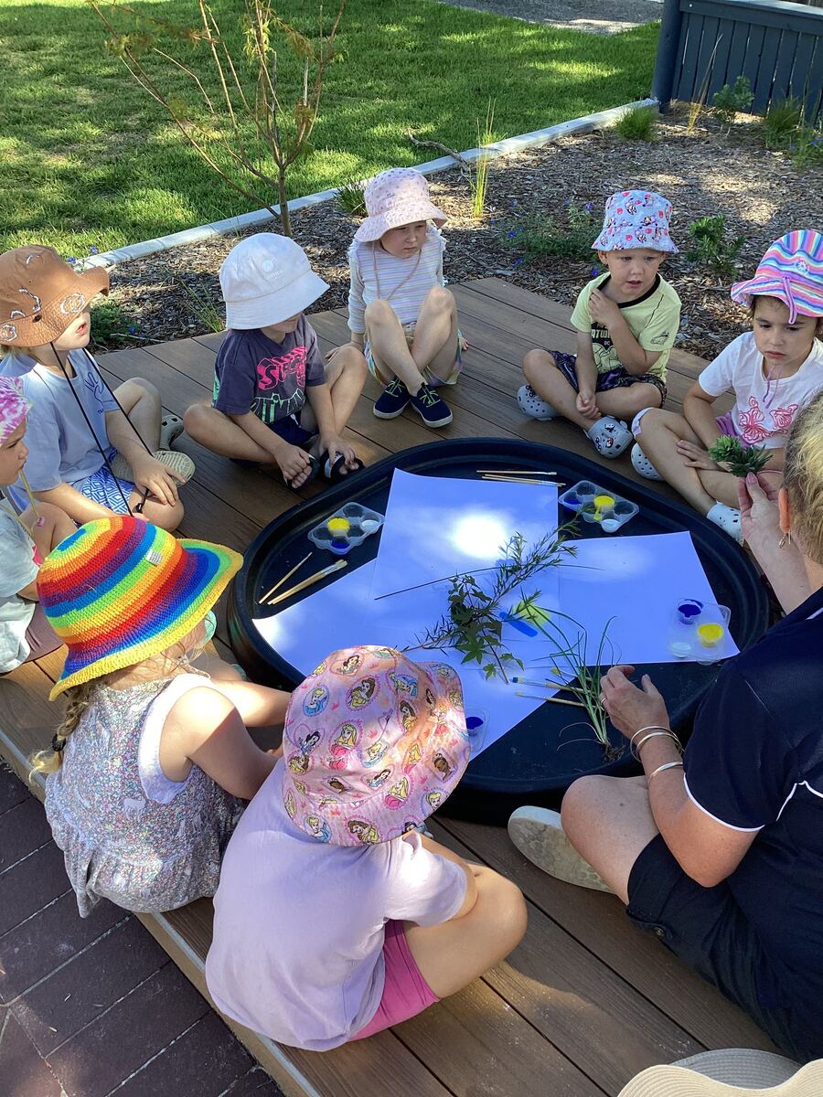 Children sit around a table for an outdoor art activity with educators