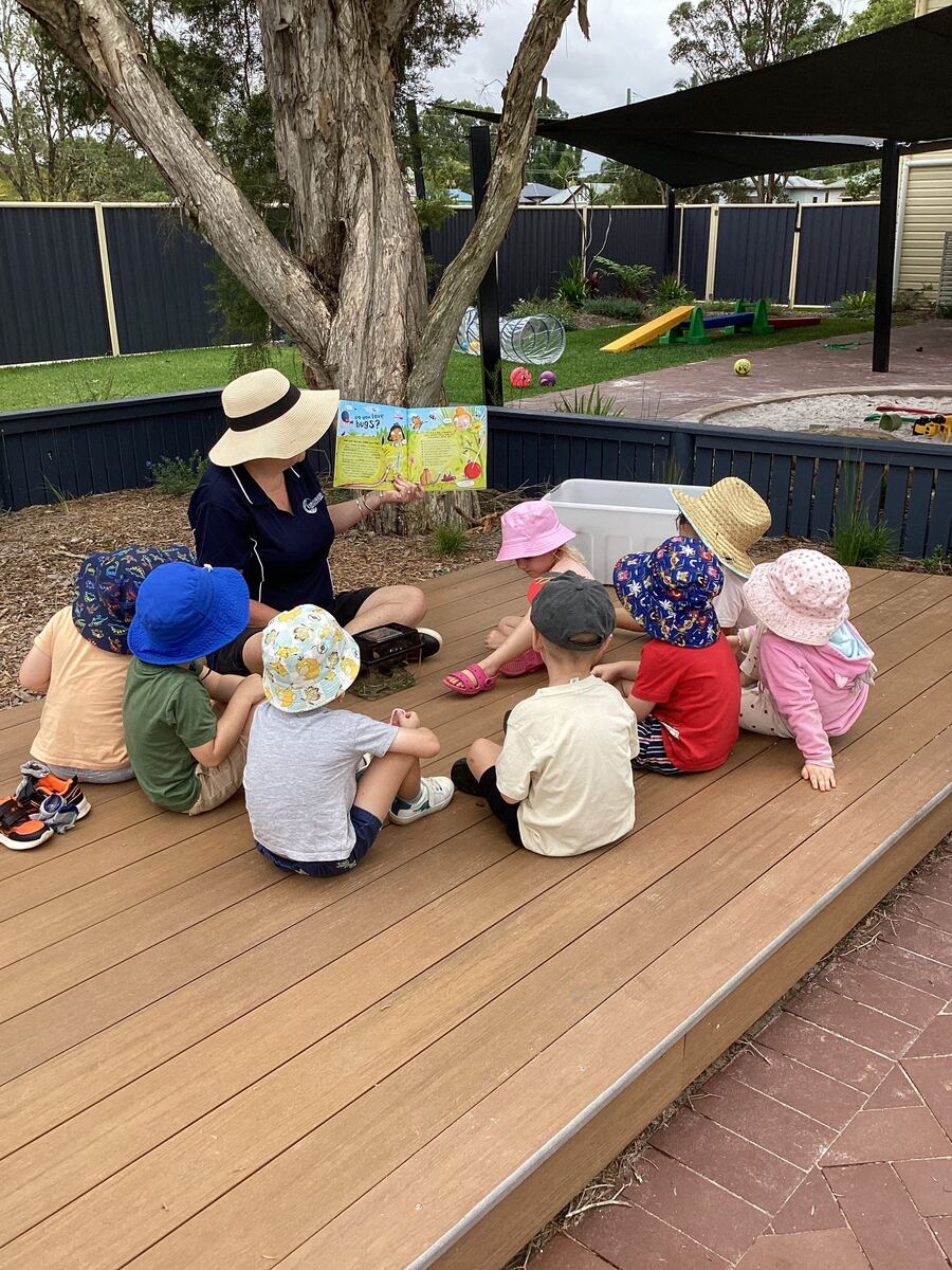 An educator reads to toddlers seated on an outdoor deck