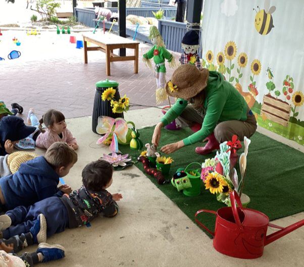 An educator shows freshly picked flowers to children seated in the garden