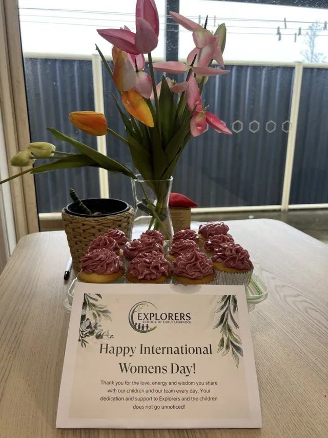 Cupcakes with rose-pink frosting and tulips beside an Explorers International Women's Day card